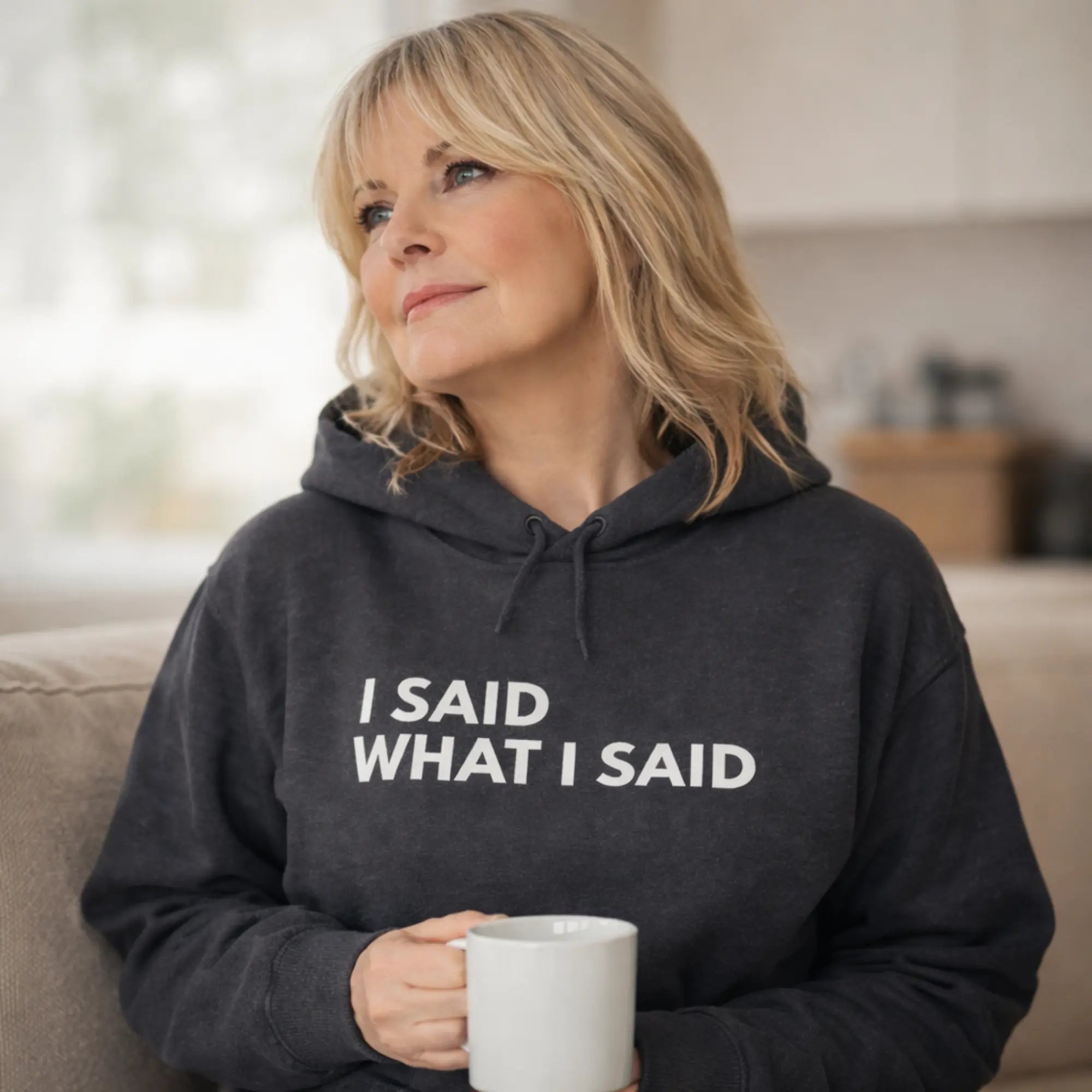 middle aged UK woman wearing dark heather “I said what I said” hoodie holding coffee mug