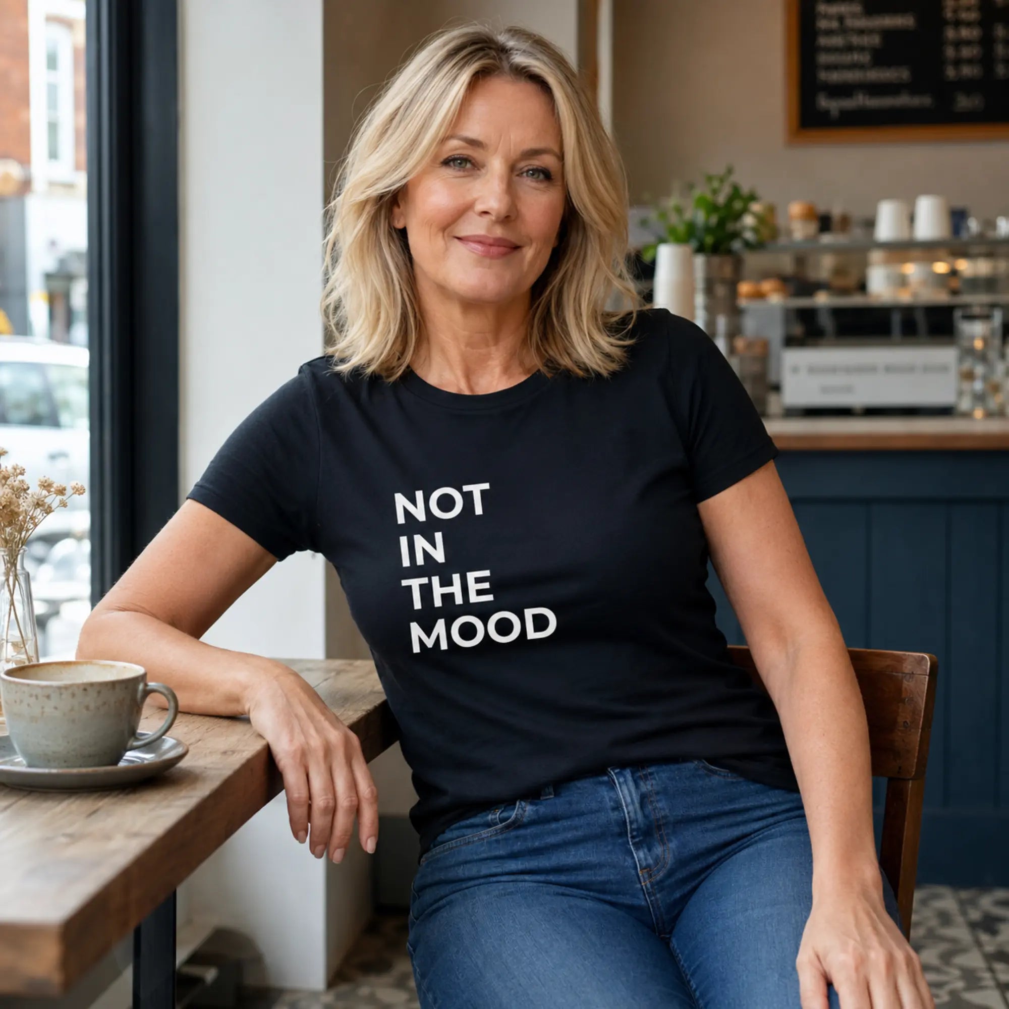 Woman wearing Not In The Mood black slogan t-shirt in a stylish café
