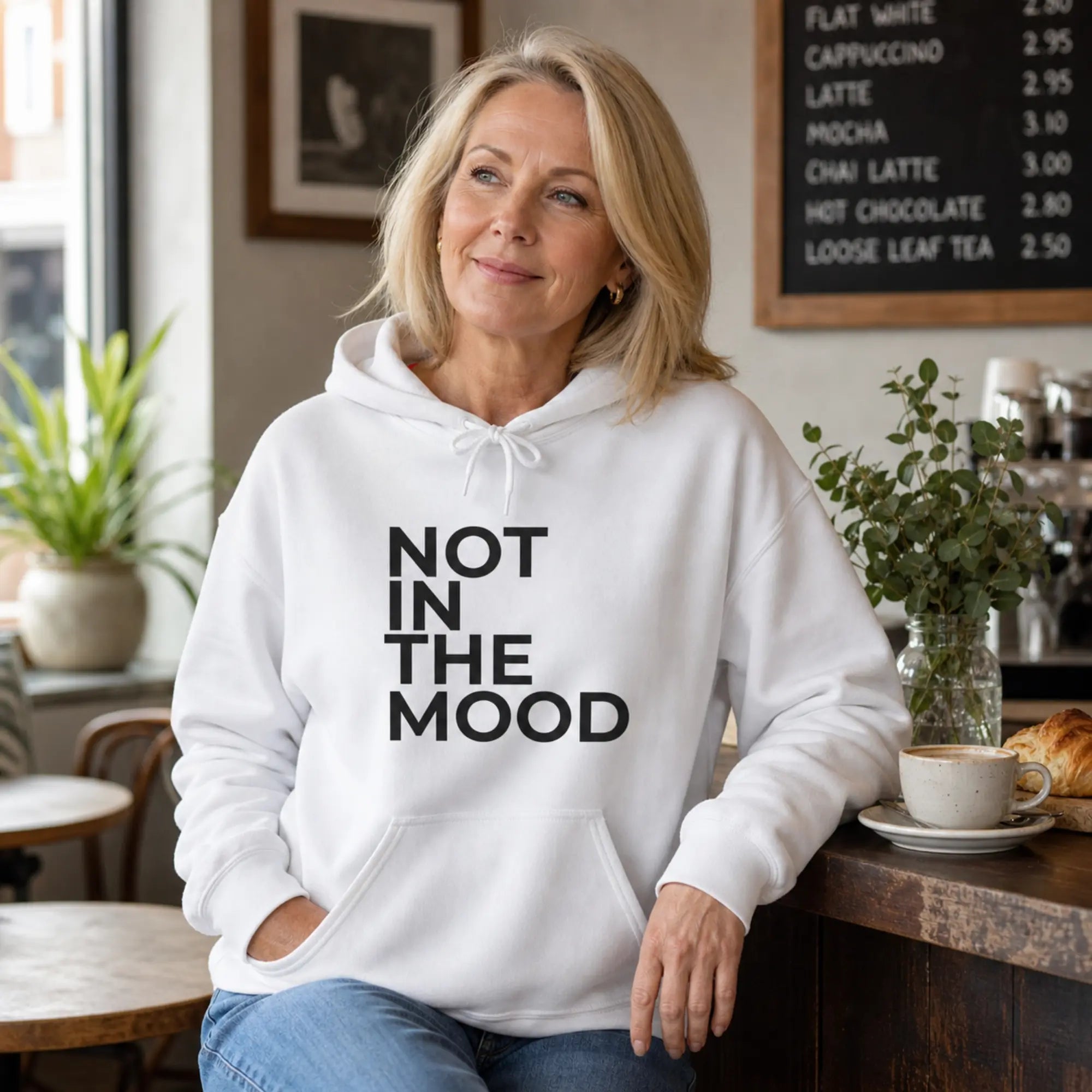 Woman wearing Not In The Mood white slogan hoodie at home with jeans