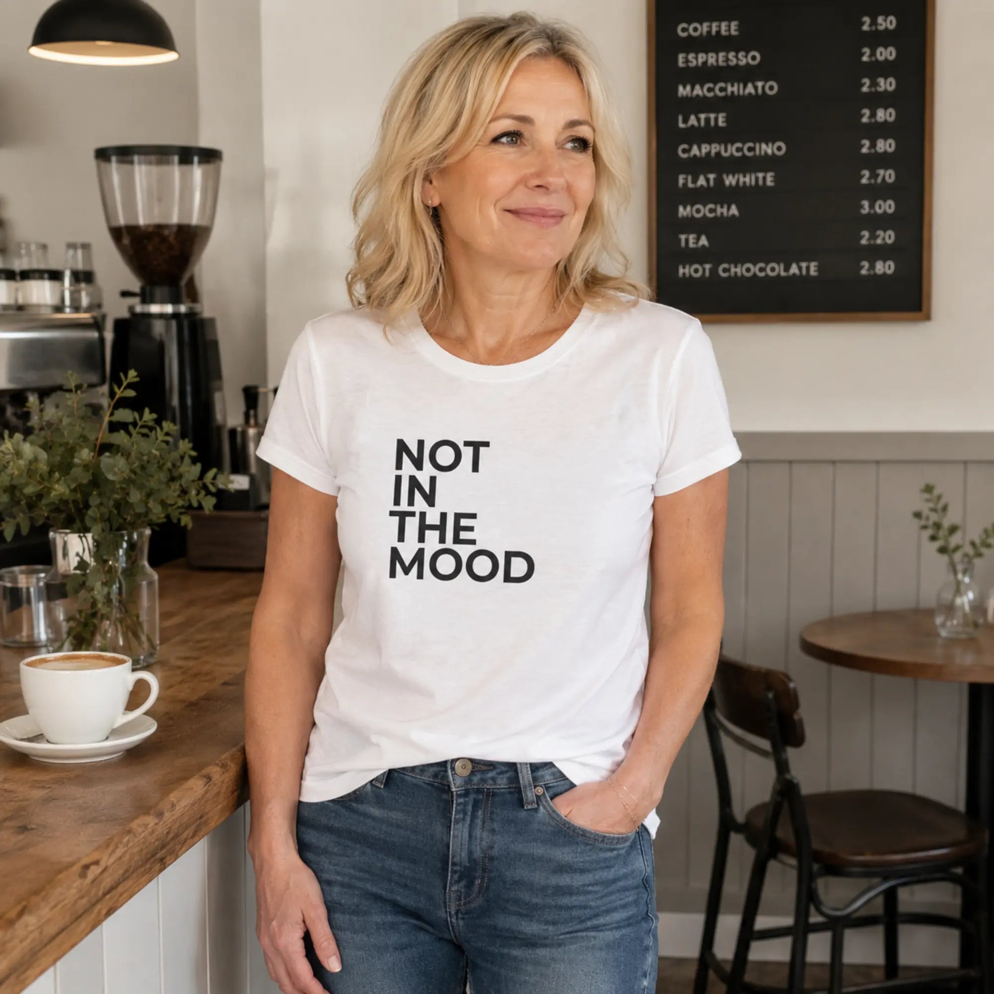 Woman wearing Not In The Mood white slogan t-shirt in a stylish café